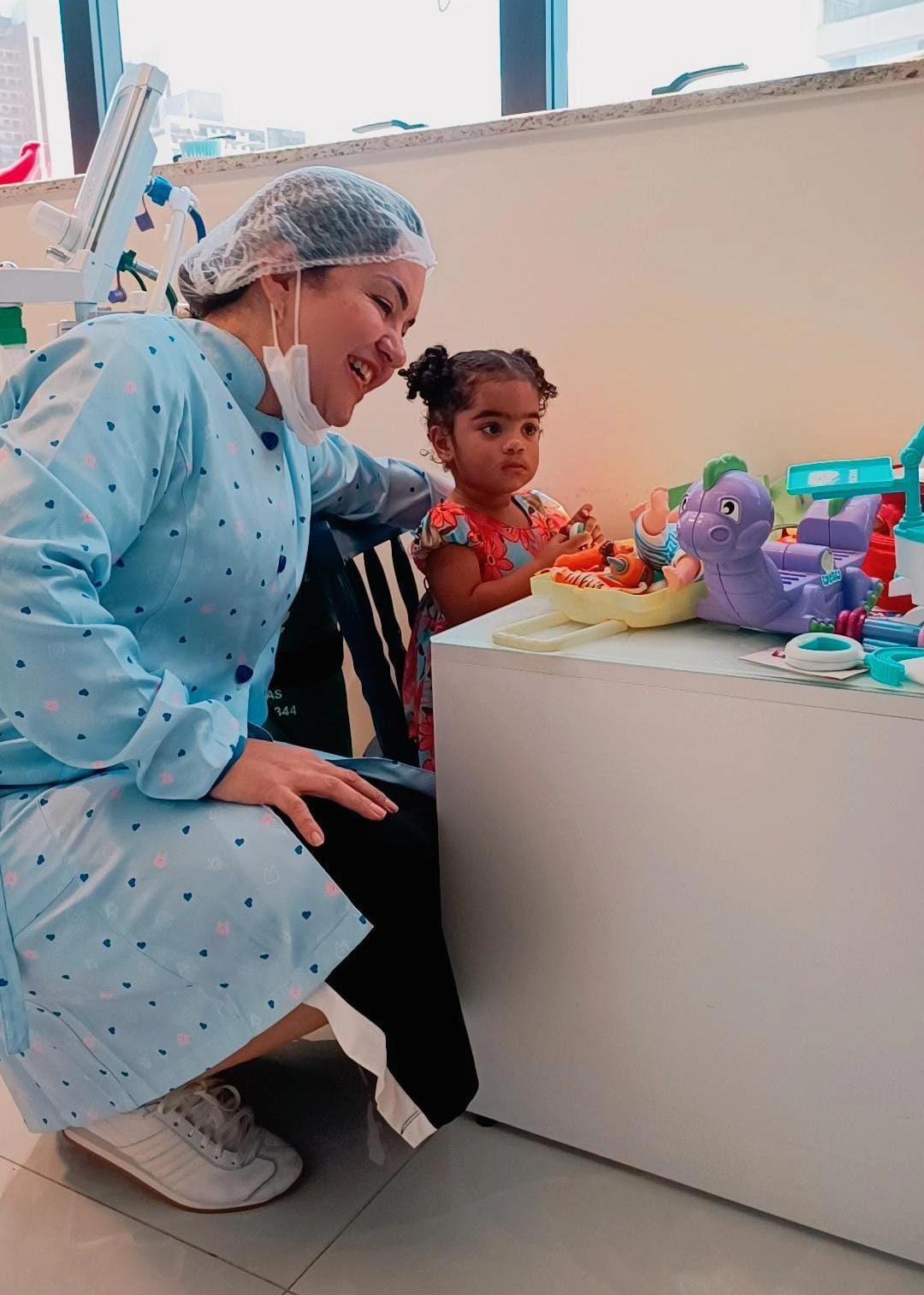 Dentista brincando com criança pequena em consultório odontológico infantil