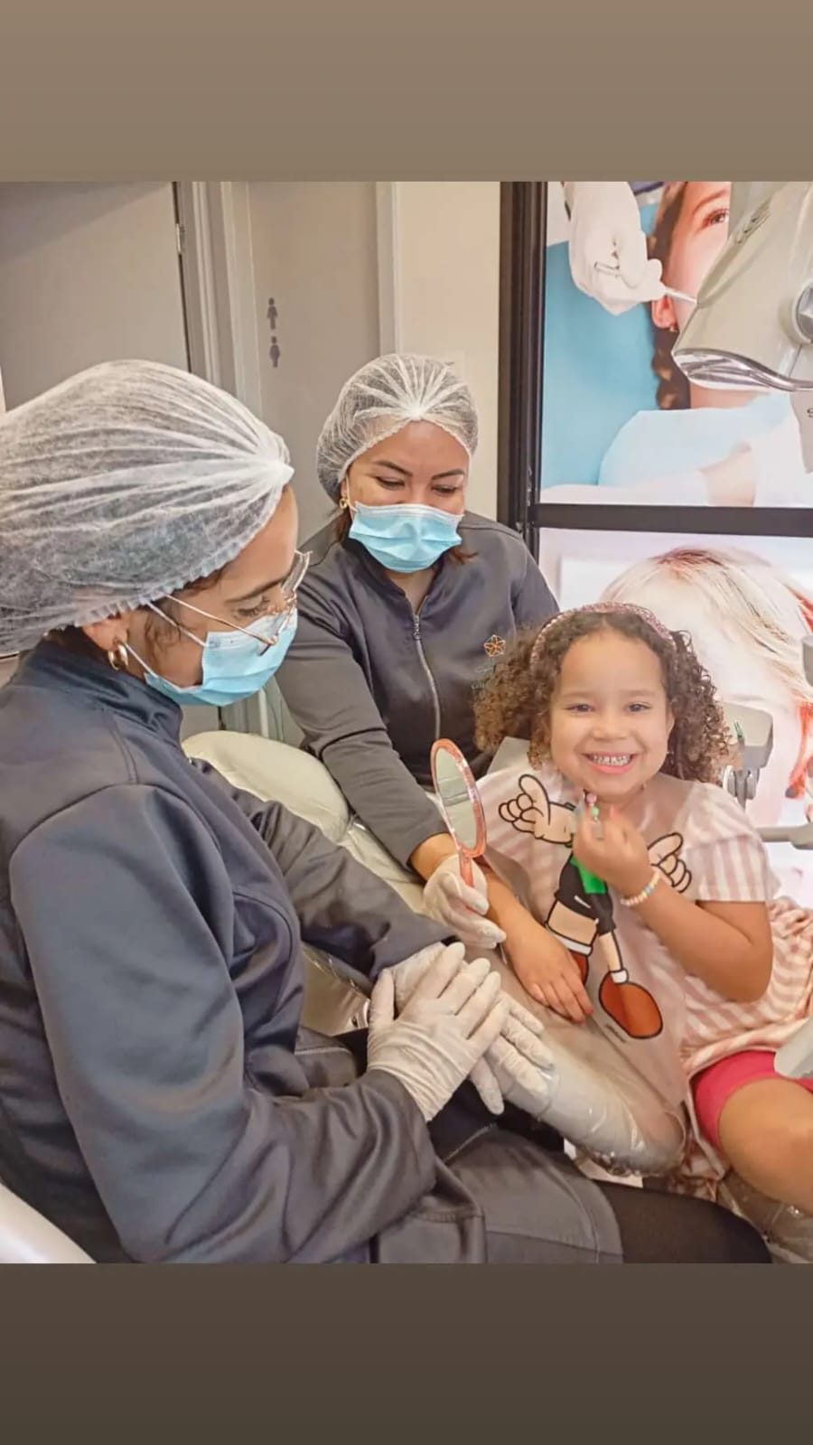 Criança sorridente segurando espelho durante consulta odontológica